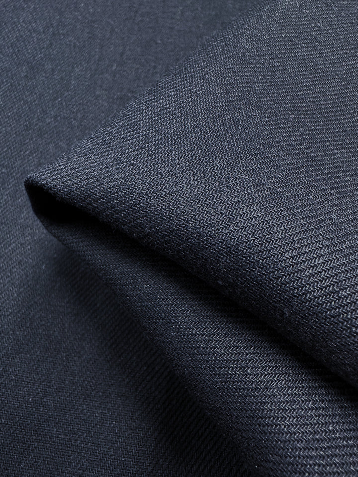 Close-up of Indonesia Ink Pure Washed Linen - 140cm by Super Cheap Fabrics reveals a durable, tightly woven dark gray texture with intricate details, ideal for crafting quality garments.