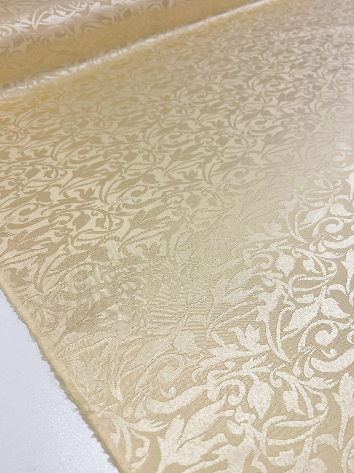 A detailed view of the Designer Damask - Rutabaga from Super Cheap Fabrics, with its intricate floral pattern featuring swirling vines and leaves that contribute to its textured and luxurious appearance.