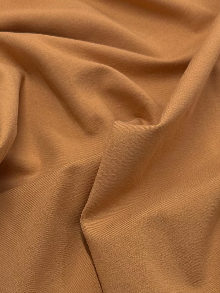 A close-up of Super Cheap Fabrics' Cotton Lycra in Caramel (165cm) reveals a soft, medium-heavy weight fabric with gentle folds and creases for a smooth, textured look.