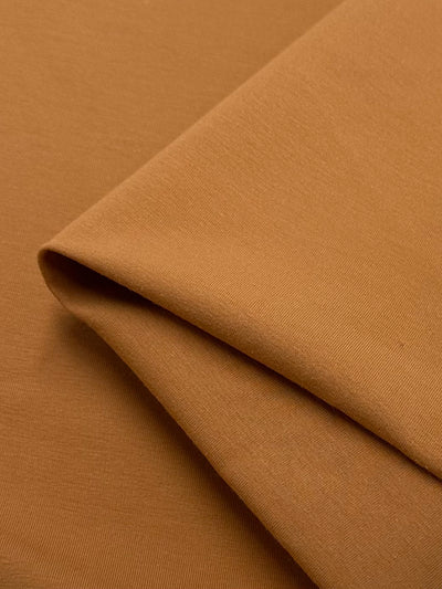 A close-up of neatly layered Super Cheap Fabrics' Cotton Lycra in Caramel, featuring a smooth texture. This medium-heavy weight fabric, measuring 165cm wide, presents a clean and orderly appearance.