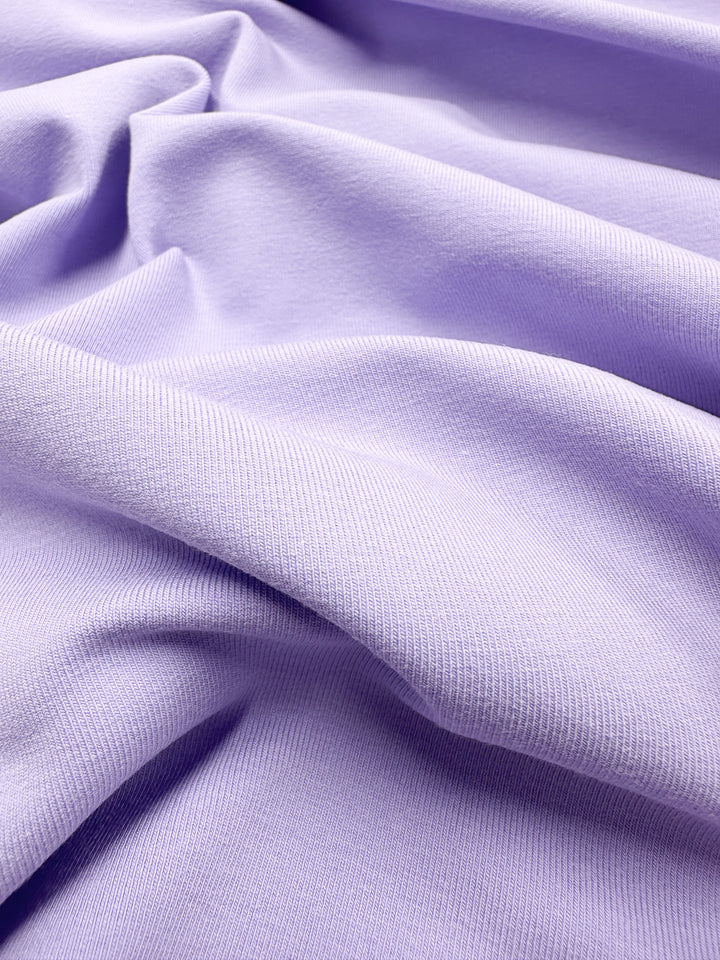 Close-up of medium-heavy Cotton Lycra - Purple Rose by Super Cheap Fabrics, 165cm wide. The lavender fabric features gentle folds and a ribbed texture, showing smoothness and subtle light-shadow variations across its breathable surface.