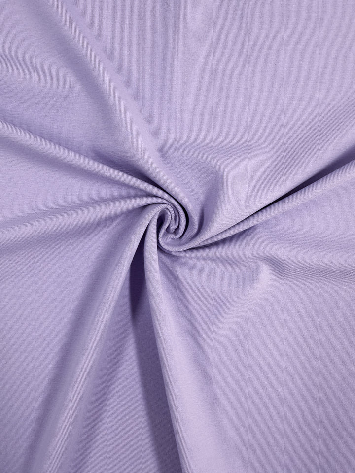 Close-up of Super Cheap Fabrics' Cotton Lycra - Purple Rose, 165cm with a textured spiral at the center. The breathable, soft, light purple fabric swirls outward in gentle folds, creating a captivating effect.