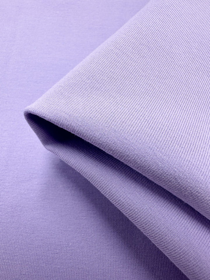 A folded piece of Super Cheap Fabrics' Cotton Lycra in Purple Rose (165cm) rests on a matching background, showcasing its seamless fine ribbed texture. This breathable, medium-heavy weight fabric offers both elegance and comfort.