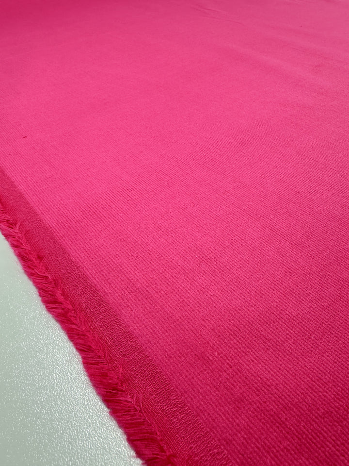 A close-up of Micro Wale Corduroy in Beetroot Purple by Super Cheap Fabrics, 137cm wide, with a slightly ribbed texture and frayed threads along one edge, ideal for winter clothing.