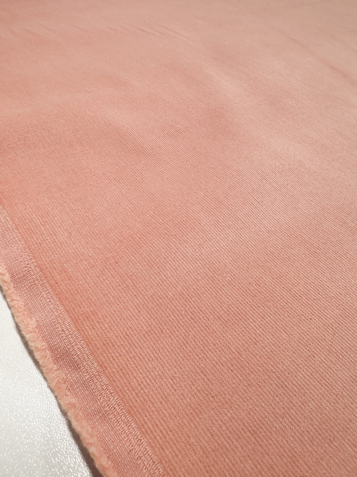 Close-up of Super Cheap Fabrics' Micro Wale Corduroy in peach, 145cm wide, showcasing a soft, plush surface with a smooth ribbed texture and a discreet seam on the left. Ideal for cozy winter apparel.