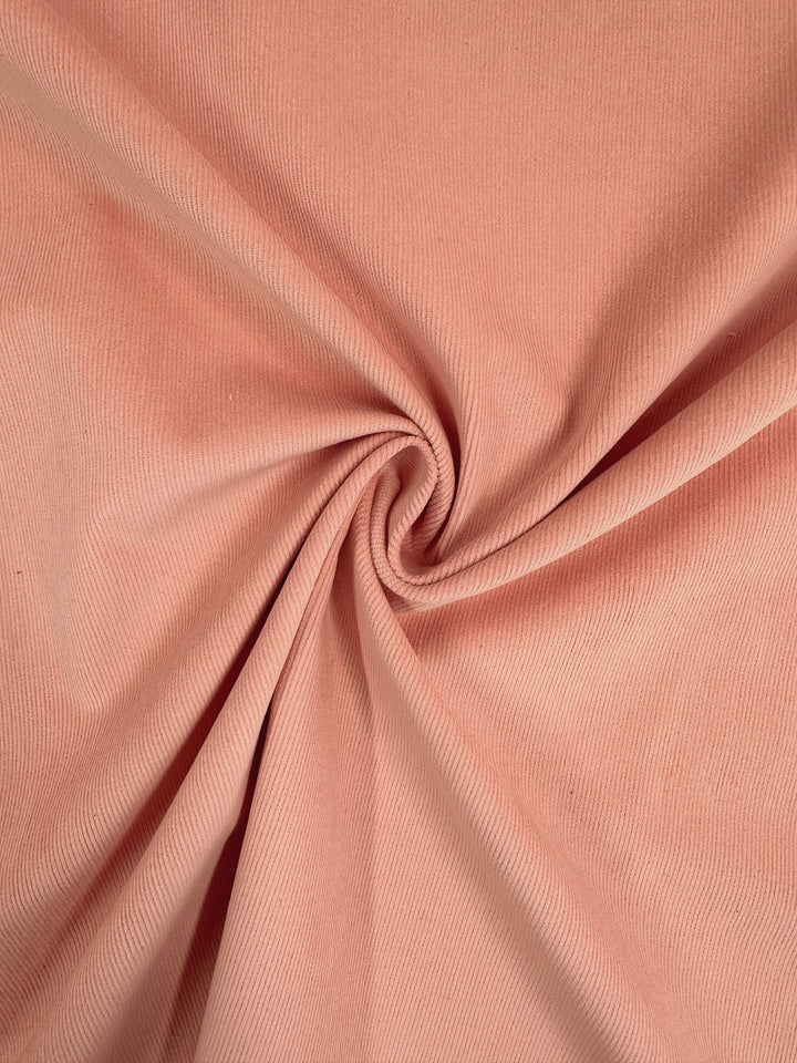 The Micro Wale Corduroy in Peach by Super Cheap Fabrics has a smooth, swirling ribbed texture that forms gentle folds and shadows, enhancing its elegant appearance. This 145cm fabric is perfect for crafting cozy winter clothing.