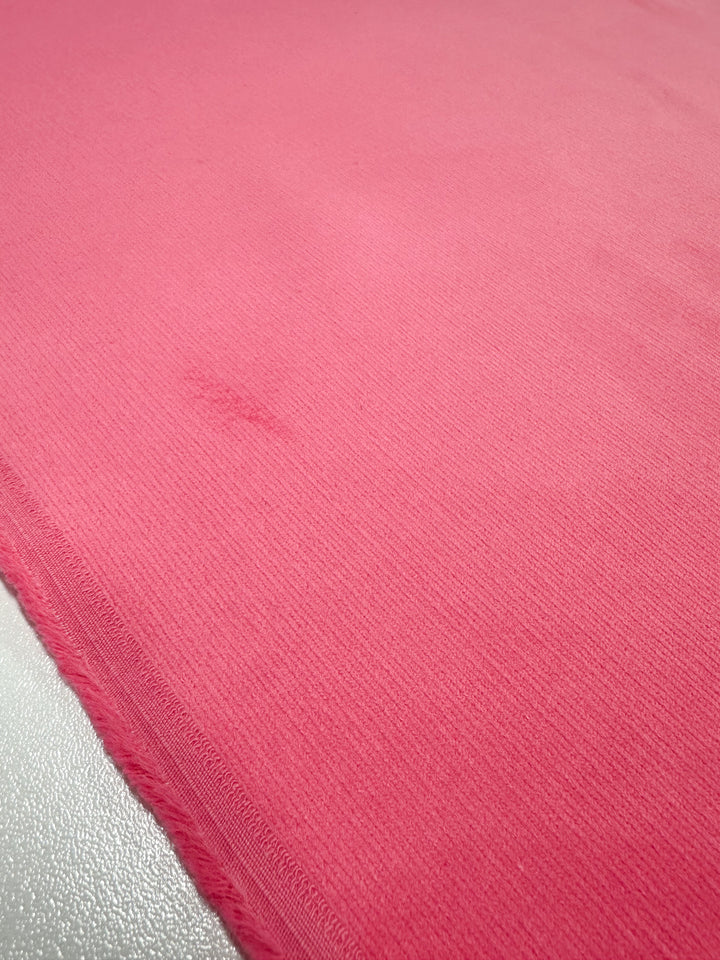 Close-up of the Micro Wale Corduroy - Camellia Rose fabric by Super Cheap Fabrics, showcasing its ribbed texture and slight imperfections over a metallic surface. The 147cm wide material has a soft, cozy appearance with visible edge stitching.