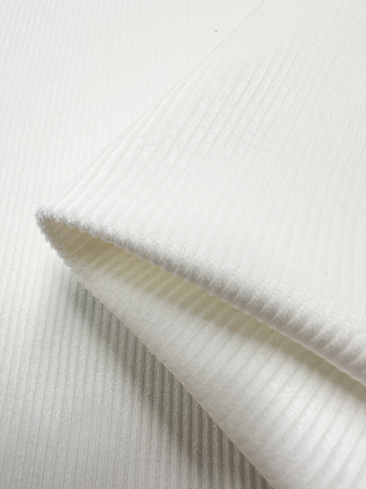 Close-up of Super Cheap Fabrics' Pin Wale Corduroy in Ivory, 150cm wide, displays its ribbed texture with small, evenly spaced vertical ridges. The softly highlighted edges and folds emphasize the fabric's smoothness and quality.