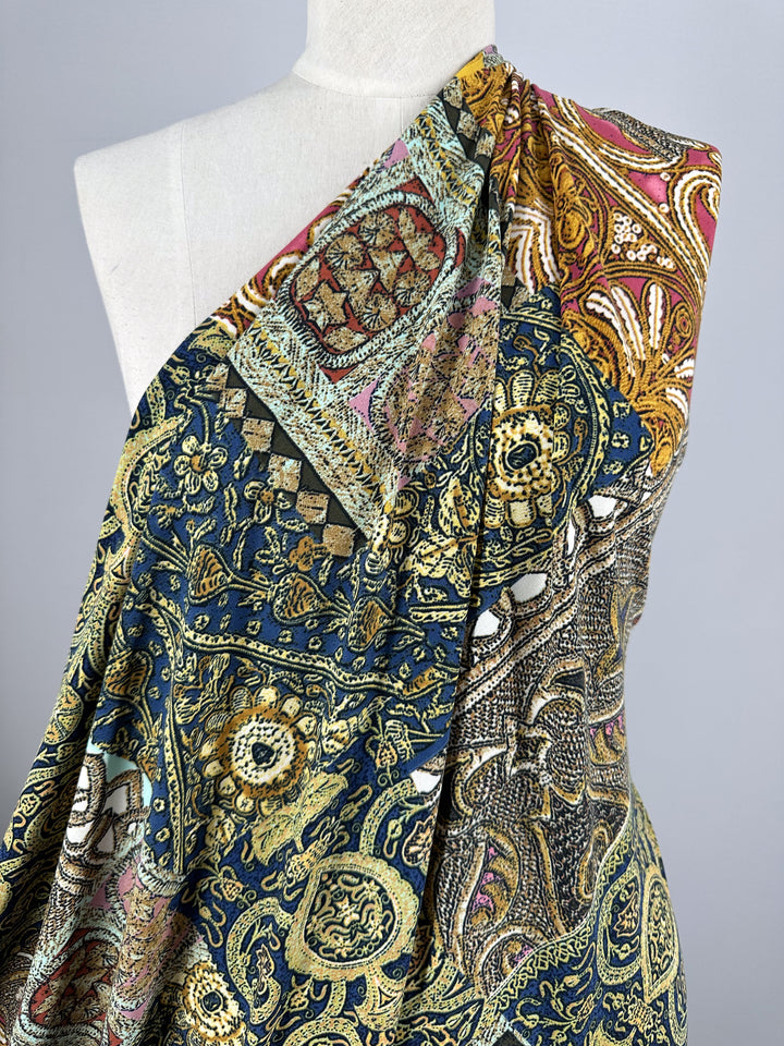 A mannequin is draped with Super Cheap Fabrics' Printed Lycra - Mosaic Patchwork, a medium-weight, 150cm fabric featuring an intricate mix of gold, blue, and red floral and paisley designs for a rich appearance.