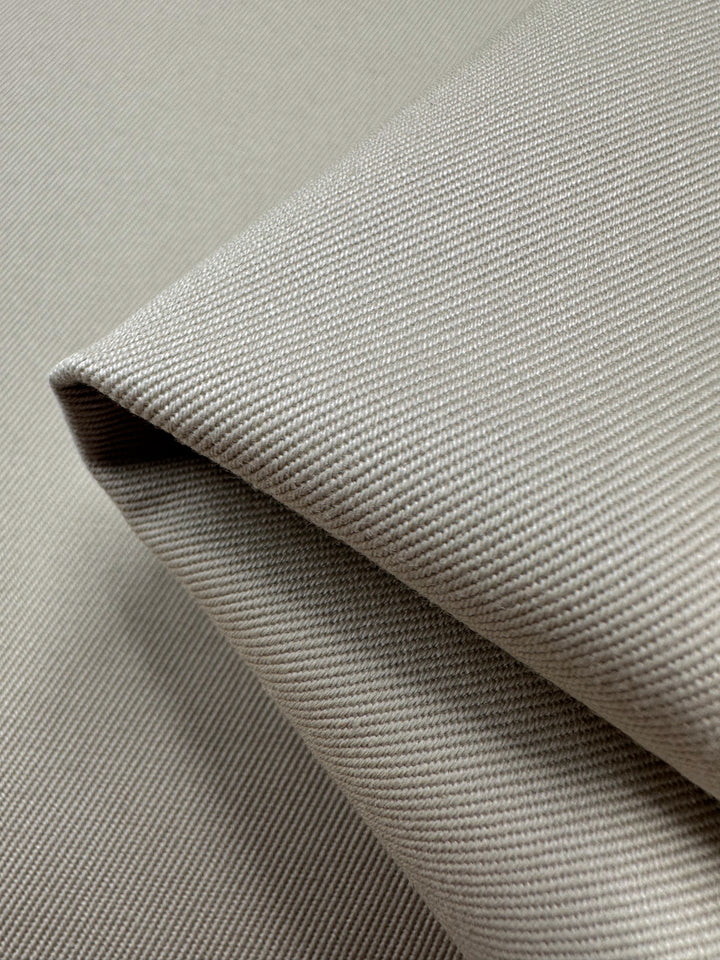 Close-up of a neatly folded piece of linen drill fabric named "Ancient Scroll - 140cm" from Super Cheap Fabrics, showcasing its light gray color and smooth weave texture, highlighting the fabric's surface details, thickness, and quality.