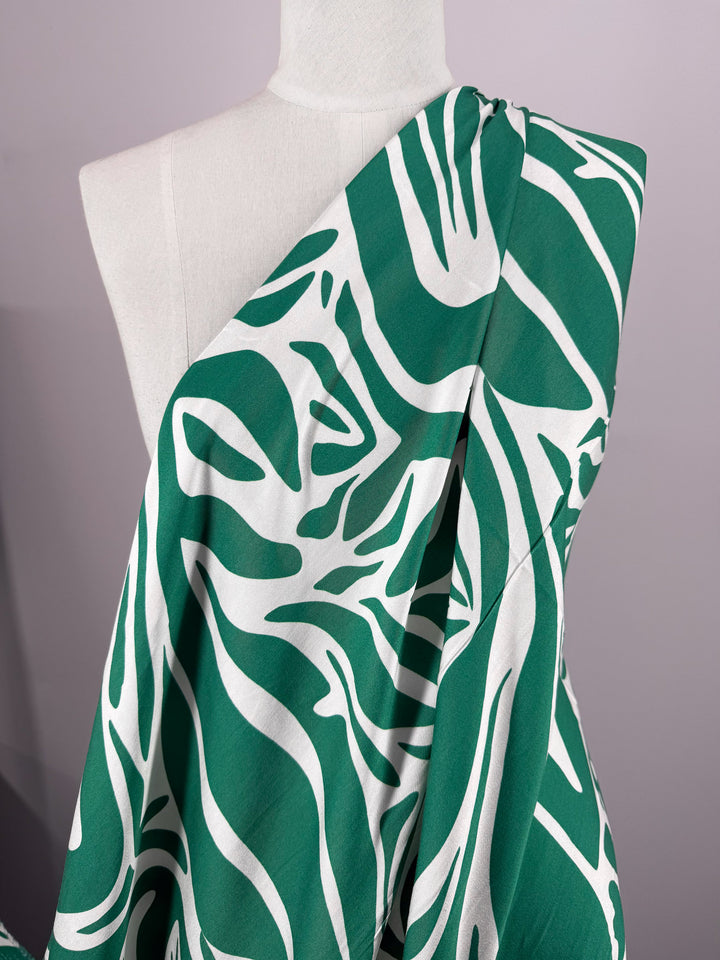 A white mannequin displays Super Cheap Fabrics’ Mercerised Rayon - Tropic Cutout - 150cm, featuring a bold green and white abstract zebra stripe pattern. The breathable rayon stands out against a softly lit plain background.
