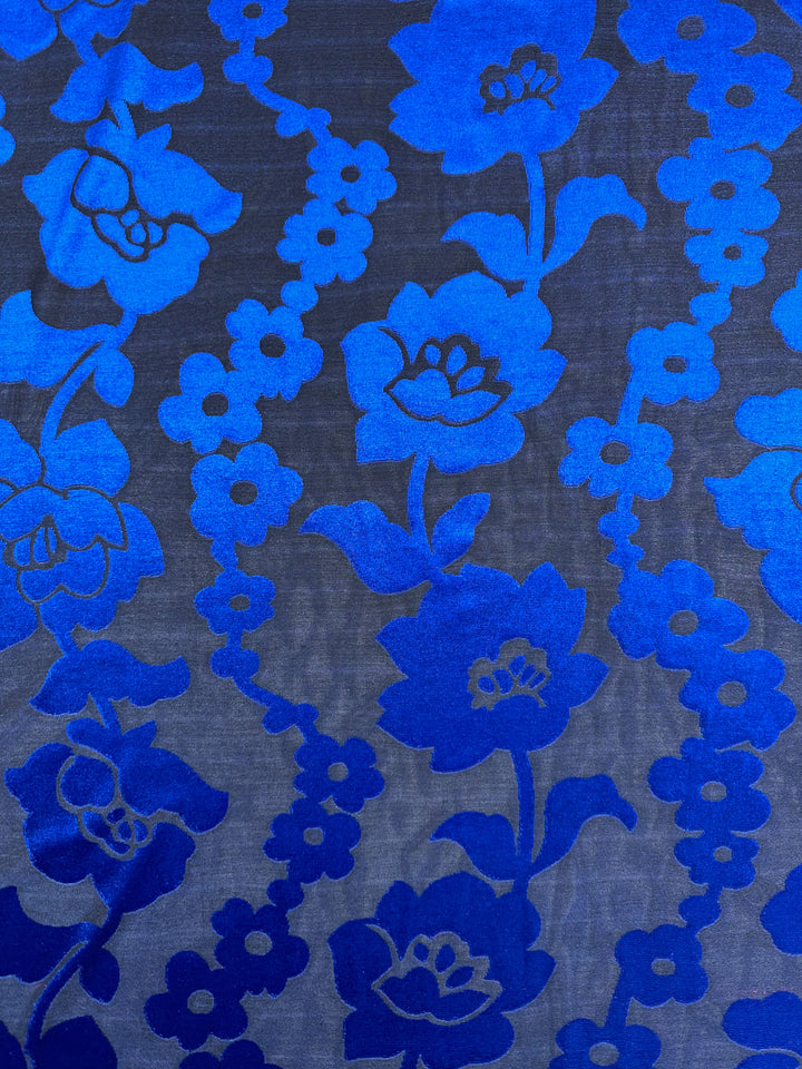 This luxurious Super Cheap Fabrics' Burnout Velvet - Snorkel Blue (155cm) showcases a vibrant pattern with large blue flowers and vines on a dark backdrop, using varied blue shades to enhance depth and texture.