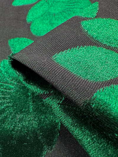 A close-up of Super Cheap Fabrics' Burnout Velvet - Amazon - 150cm displays a sophisticated style with its luxurious black base and large, textured green leaf patterns, highlighting intricate detailing and contrasting colors.