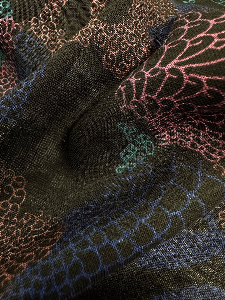 Close-up of Linen Blend - Coral by Super Cheap Fabrics, highlighting its intricate swirling patterns in pink, green, and blue on a multi-black background. The textured 147cm fabric appears gently draped, showcasing the detailed and colorful embroidery.