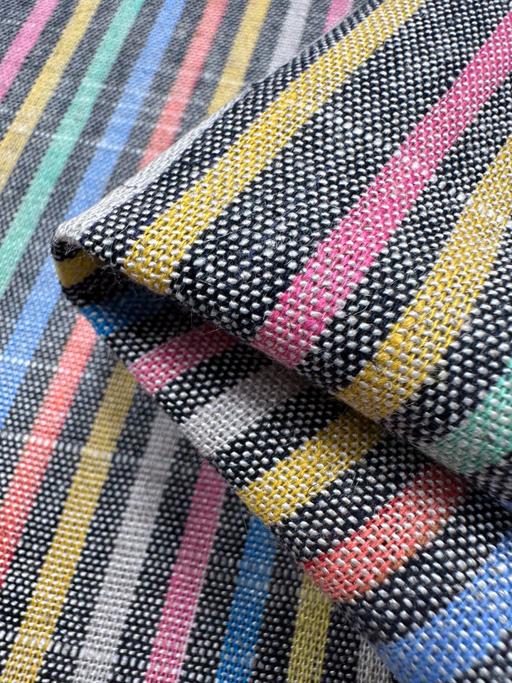 A close-up image showcases folded woven fabric from Super Cheap Fabrics' Linen Blend - Beachside (143cm), featuring colorful stripes in black, yellow, blue, pink, and gray. The texture and weave pattern highlight its intricate vintage design.