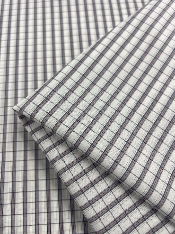 Close-up of Shirting - Dave - 147cm by Super Cheap Fabrics, showcasing folded polyester fabric with a checkered pattern of thin blue and black lines on a white background. The lightweight material has a smooth texture and is neatly arranged.