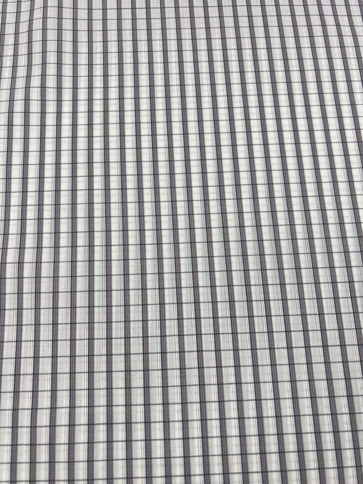 A close-up of the Shirting - Dave - 147cm from Super Cheap Fabrics displays a grid pattern of intersecting lines, creating small squares. The dark lines form a uniform, repetitive design against a light background, resembling lightweight fabric.