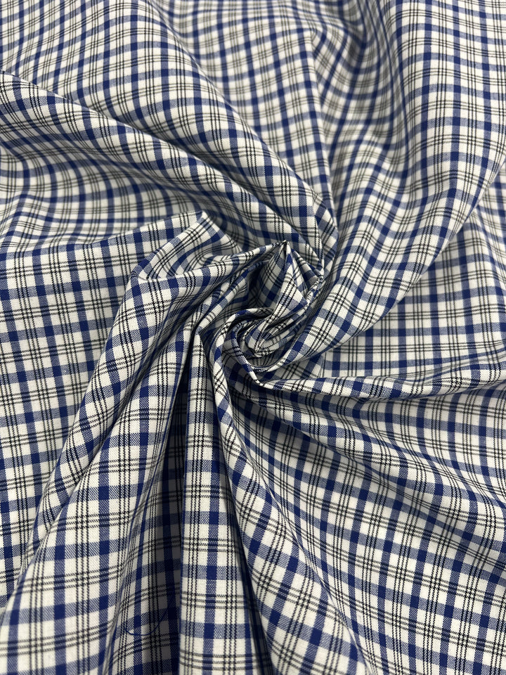 Close-up of crumpled Shirting - Roy fabric by Super Cheap Fabrics, made from a lightweight polyester-cotton blend in a blue and white plaid pattern. Gathered at the center, it adds texture and depth, ideal for children's wear designs.