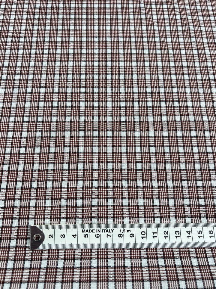 A close-up of Terra shirting fabric in a brown and white checkered pattern features a measuring tape at the bottom, displaying measurements in centimeters to highlight pattern size. Made from polyester cotton, the Super Cheap Fabrics label reads "MADE IN ITALY.