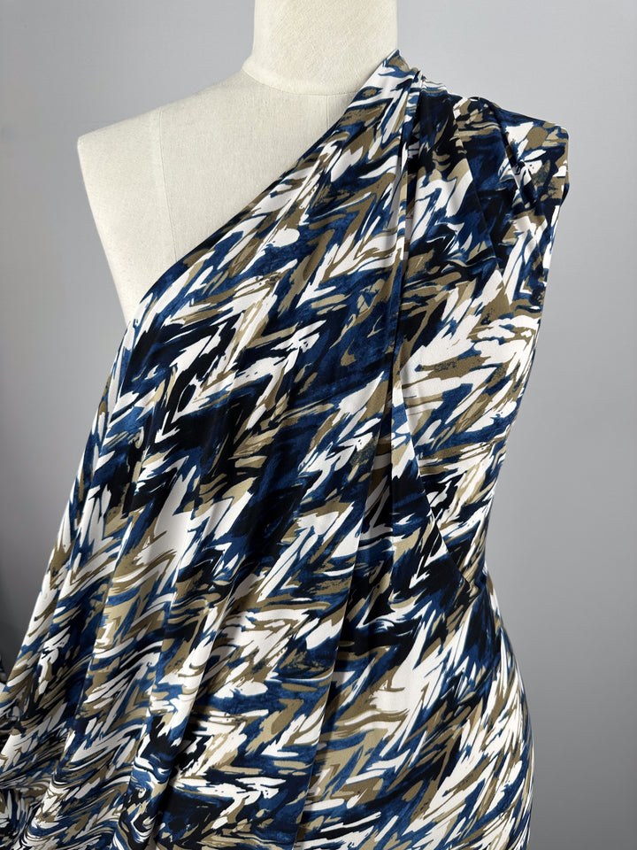 A mannequin displays Super Cheap Fabrics' Printed Lycra - Arrows, a medium-weight polyester/spandex blend featuring an abstract blue, white, and brown pattern in a chic one-shoulder design.