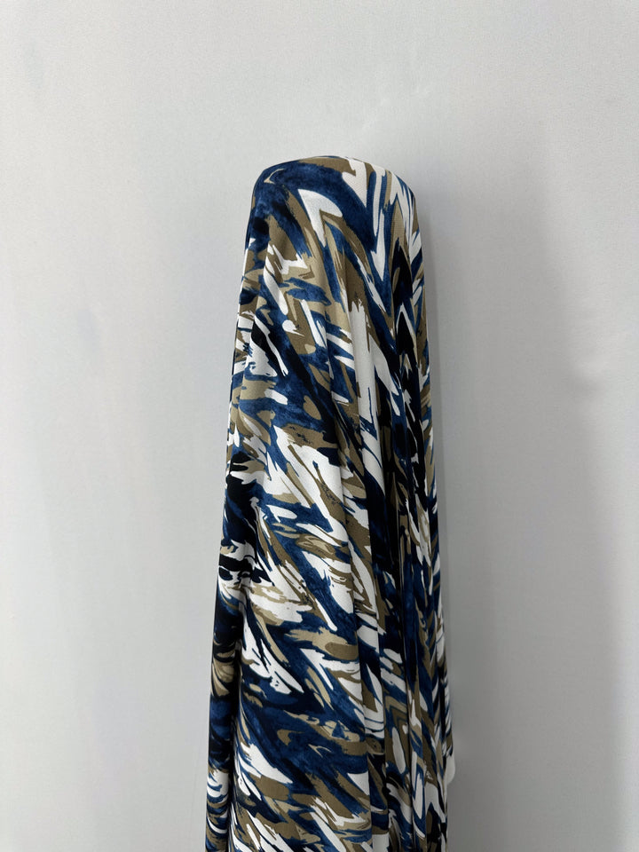 A medium-weight, 150cm Printed Lycra fabric from Super Cheap Fabrics with an abstract pattern of blue, white, and brown arrows drapes over an unseen object against a plain gray background.