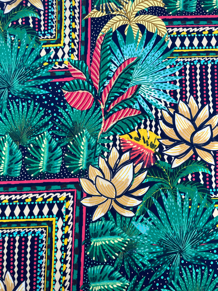 The "Printed Lycra - Palm Springs - 150cm" by Super Cheap Fabrics showcases a vibrant tropical design on medium-weight polyester/spandex, with large green leaves, yellow and pink flowers, geometric shapes, stripes, and dots for a lively effect.