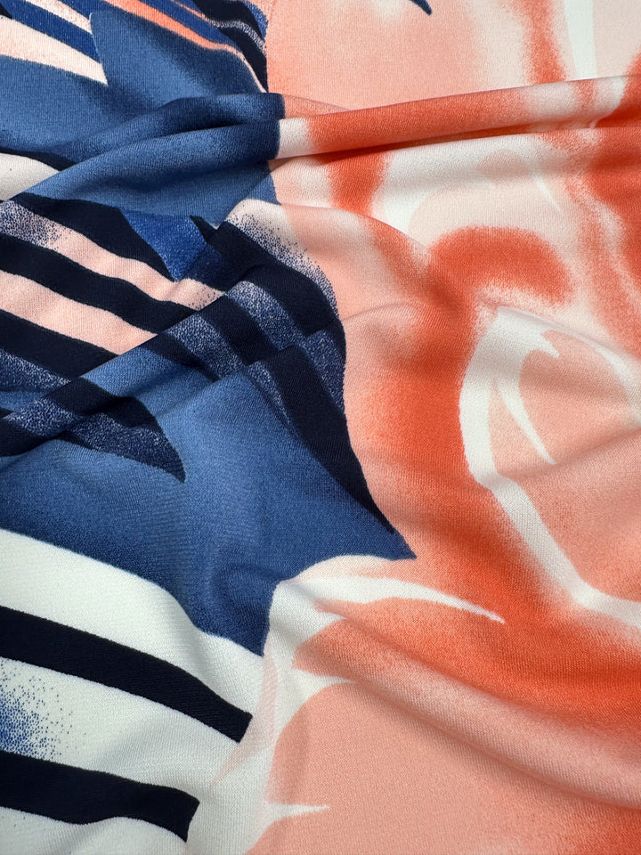 A close-up image of the Super Cheap Fabrics' Printed Lycra - Bold - 150cm reveals a medium-weight fabric with an abstract design of dark blue and white stripes contrasting flowing coral and light pink swirls, featuring a smooth texture and gentle two-way stretch.