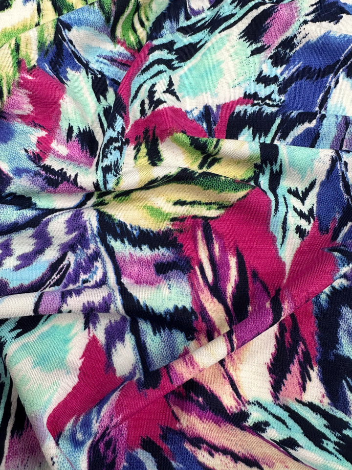 The Printed Lycra - Wavy by Super Cheap Fabrics is a vibrant, multicolored textile with abstract patterns in pink, purple, blue, green, and cream. It has a medium weight and features both jagged and smooth lines across its soft, flowing surface. Width: 150cm.