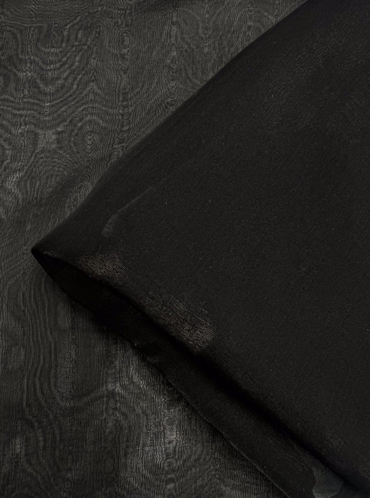 A detailed view of Super Cheap Fabrics’ Silk Mousseline in Black showcases its smooth, soft texture and delicate metallic shimmer. Gentle folds in the 140cm fabric create a sense of depth and a subtle, textured pattern that catches the light beautifully.