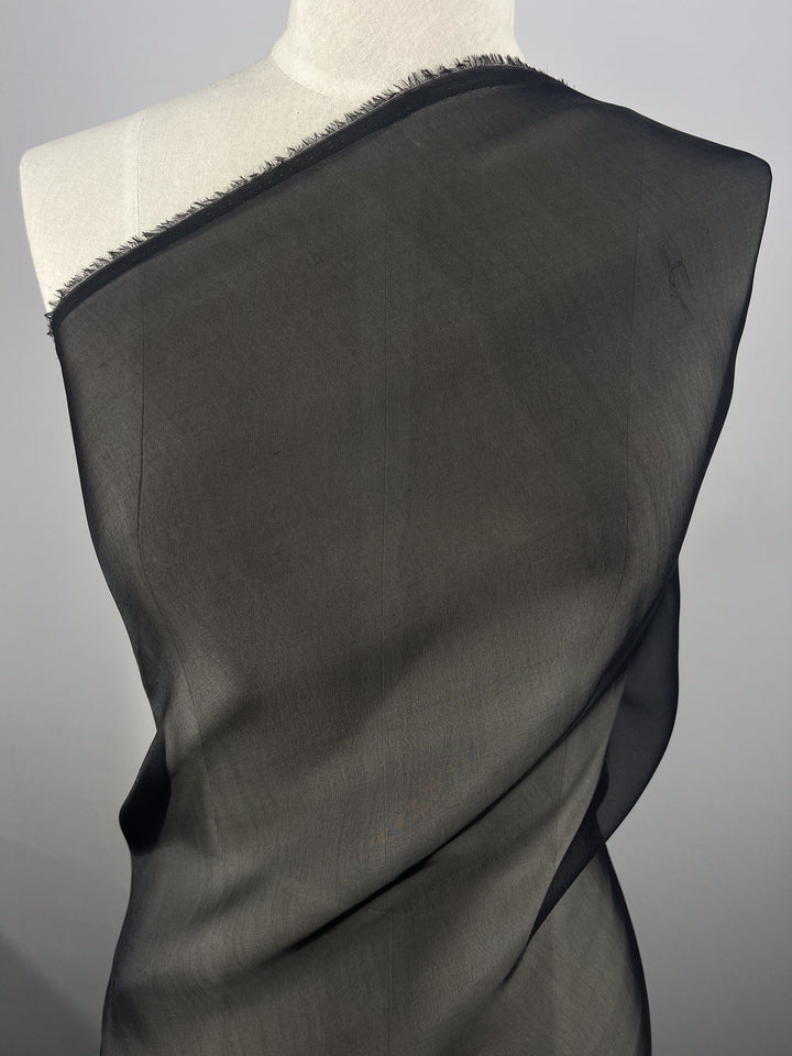 A stylish mannequin displays Super Cheap Fabrics' Silk Mousseline - Black - 140cm, draped over one shoulder to highlight its light texture and subtle metallic shimmer against a neutral backdrop.