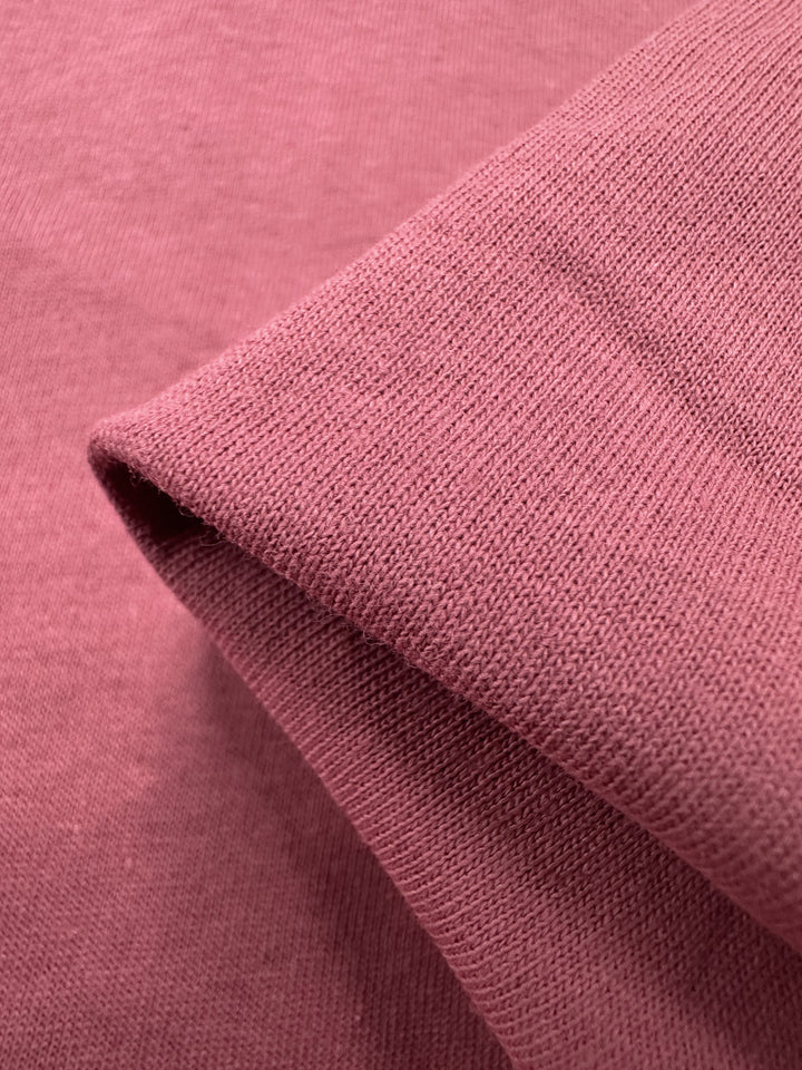 Close-up of folded Super Cheap Fabrics' Cotton Jersey - Slate Rose - 175cm, highlighting its texture and weave against a smooth surface, with contrasting folded and flat sections.