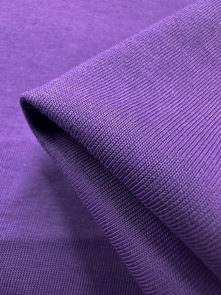 A close-up of Super Cheap Fabrics' Cotton Jersey in Patrician Purple unveils its detailed ribbed texture and medium weight. The 170cm material gracefully folded, highlights the intricate weave and rich hue.