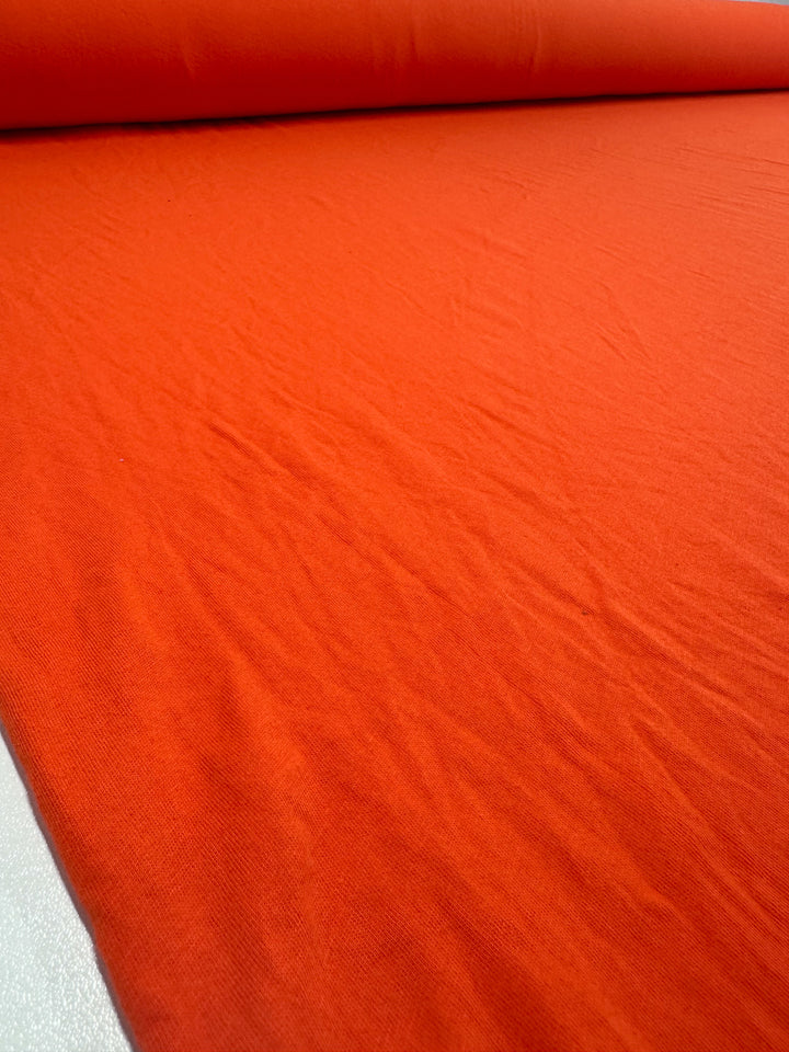 A close-up of Super Cheap Fabrics' 155cm Tangerine Tango cotton jersey shows slight wrinkles on a flat surface. The light to medium weight material looks smooth and dominates the frame.