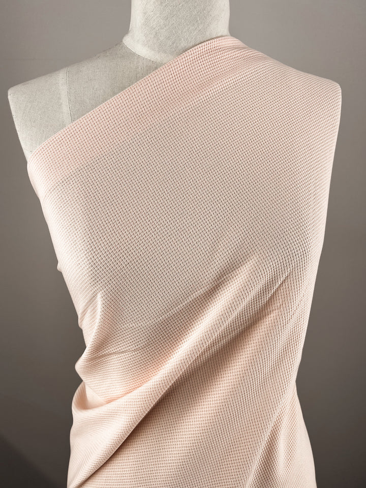 The Waffle Knit - Pearl Blush from Super Cheap Fabrics is elegantly draped over a mannequin against a neutral backdrop, highlighting the fabric's soft and refined three-dimensional texture.