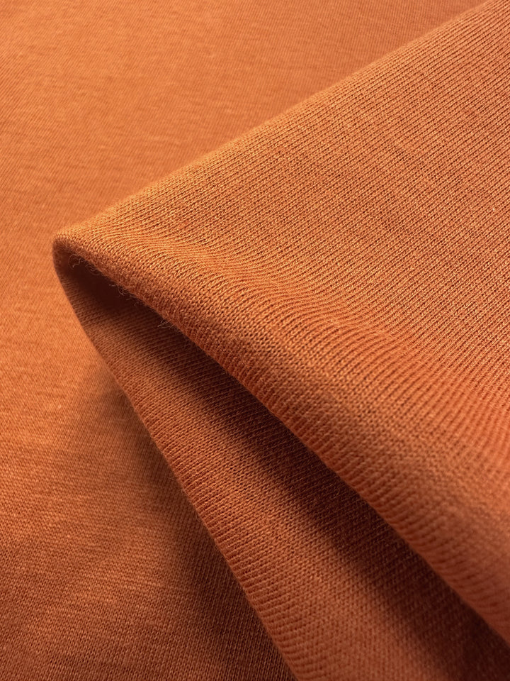 Close-up of Super Cheap Fabrics' Cotton Jersey in Apricot Orange (160cm). The fabric is soft, lightweight, and textured, showcasing a rich, warm hue.