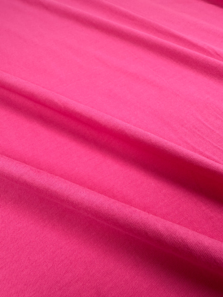 A close-up of the Cotton Jersey - Fandango Pink - 160cm by Super Cheap Fabrics, featuring gentle folds that highlight its soft texture and vibrant color.