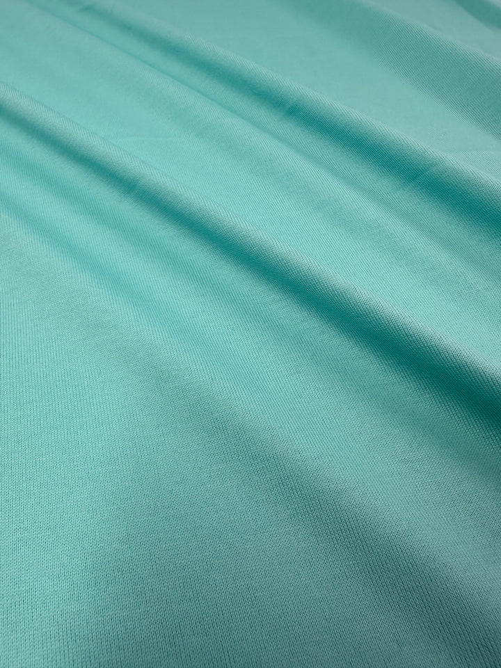 Close-up of Super Cheap Fabrics' Cotton Jersey - Aqua Splash fabric (160cm) reveals smooth, gentle folds and subtle texture. The lighting highlights its serene appearance and soft waves.