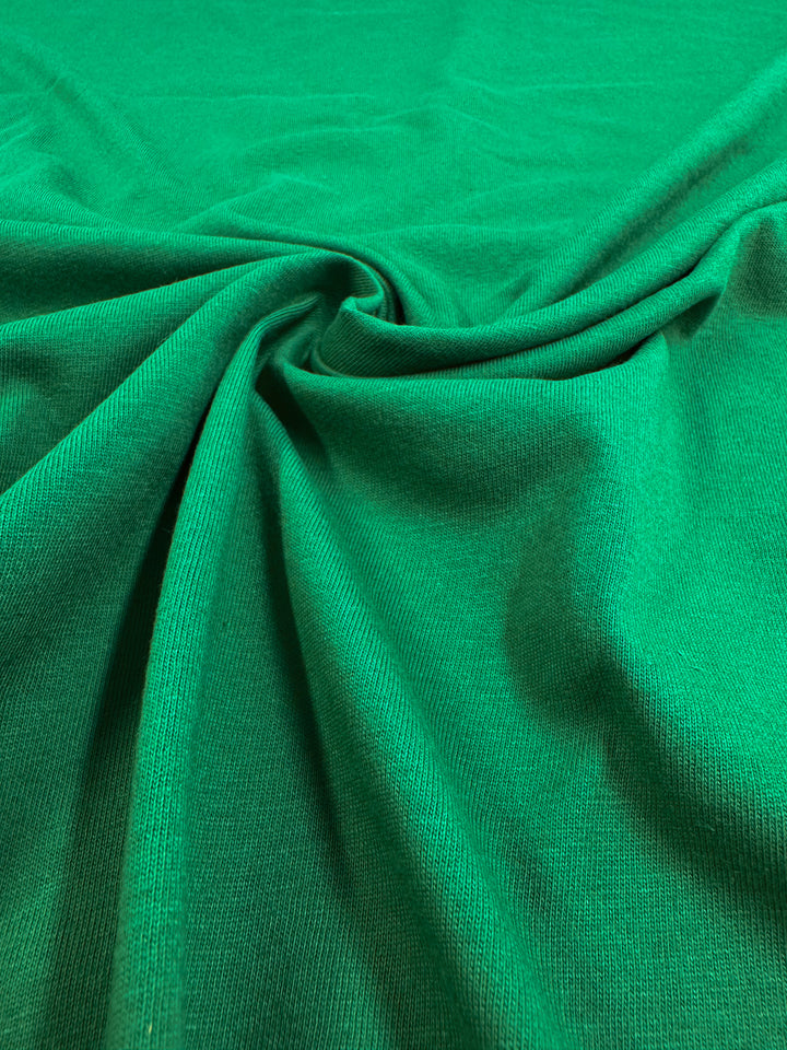 Close-up of vibrant green fabric with a smooth texture, gathered to form soft folds. This Super Cheap Fabrics lightweight jersey, named Cotton Jersey - Abundant Green - 165cm, is made from 100% cotton for comfort and style.