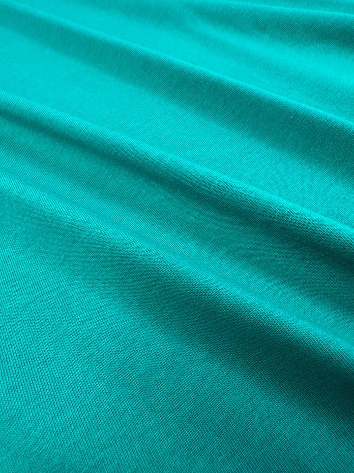 A close-up of Super Cheap Fabrics' Cotton Jersey - Kayaking - 155cm reveals teal-colored fabric with diagonal ribbing texture. The gentle folds create shadows that add depth, evocative of the flowing elegance seen in jumpsuit dresses.