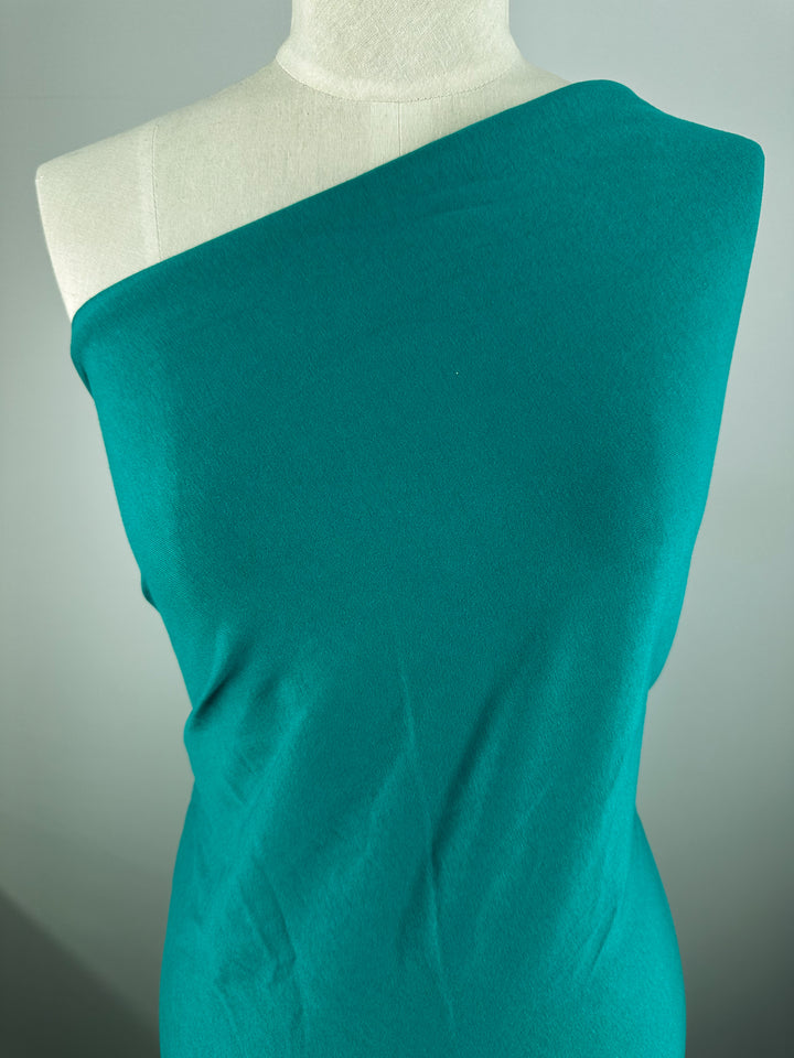 A mannequin elegantly displays the "Cotton Jersey - Kayaking - 155cm" by Super Cheap Fabrics in a teal one-shoulder design against a simple background.