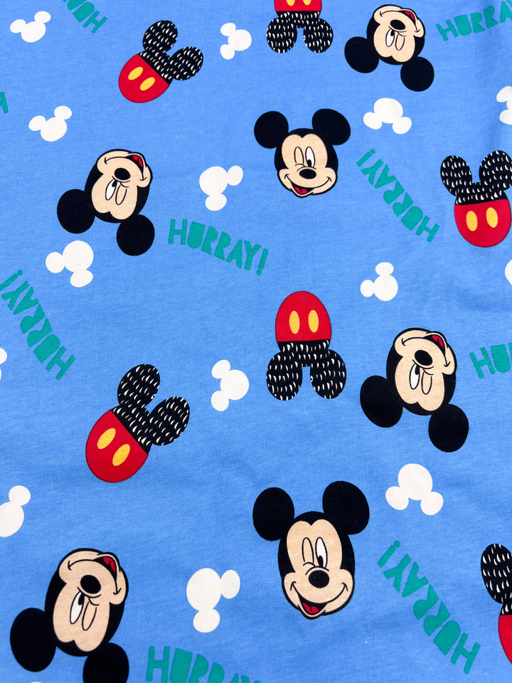 This medium-weight fabric from Super Cheap Fabrics, called the "Printed Jersey - Mickey," features a lively design with cartoon mouse faces and ears wearing red and yellow polka-dotted hats. The pattern includes white clouds surrounding the word "HURRAY!" in vibrant green, set against a blue backdrop. This fabric offers two-way stretch for extra comfort and is available at a width of 170cm.