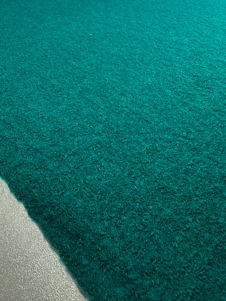 Close-up of Super Cheap Fabrics' Boiled Wool in Everglade, featuring a textured teal heavyweight fabric meeting a light gray edge with natural lighting casting subtle shadows and highlights. Width: 135cm.