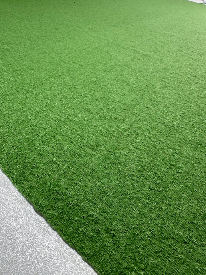 A close-up of vibrant green turf, reminiscent of the meticulous weaving found in Boiled Wool - Meadow Green by Super Cheap Fabrics, contrasts sharply with a gray concrete surface.