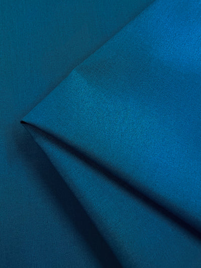 Close-up of Poplin - Celestial - 148cm by Super Cheap Fabrics, featuring folded teal fabric with a textured poly/cotton blend. The lighting emphasizes its vivid sheen and smooth depth.