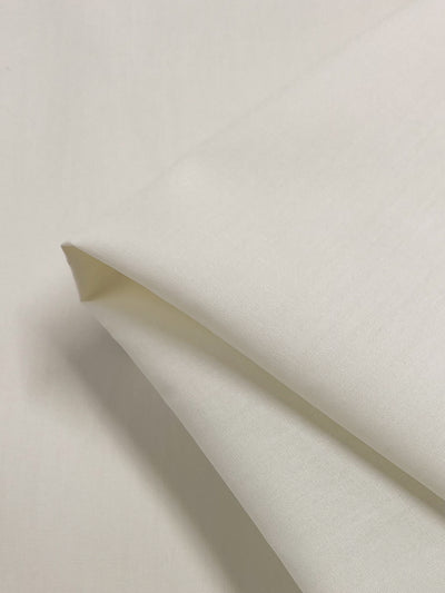 A close-up of a neatly folded, slightly textured white non-stretch fabric with clean edges and a soft feel. This polyester-cotton blend, ideal for clothing or home textiles, is the Poplin - Snow White by Super Cheap Fabrics, measuring 148cm across.