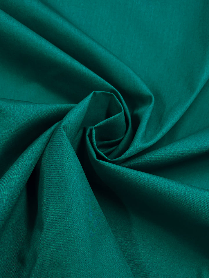 Close-up of Super Cheap Fabrics' Poplin - Kayaking (148cm), a green polyester cotton blend gracefully draped in a spiral pattern. The texture appears soft and silky, with gentle shadows that enrich the color.