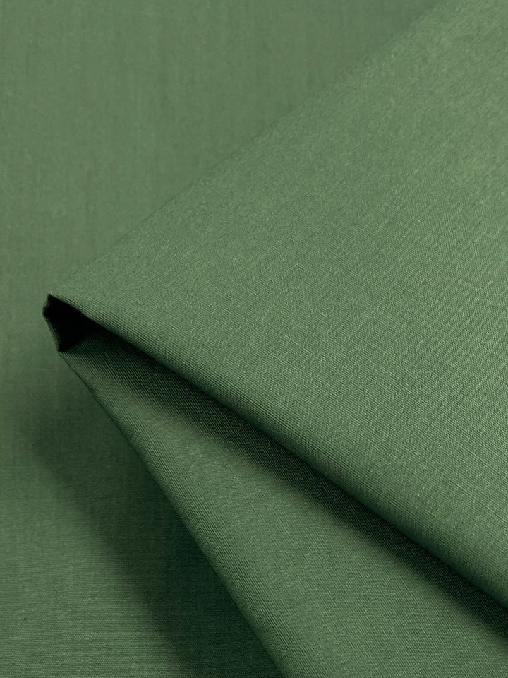 A close-up of neatly folded Super Cheap Fabrics' Poplin in Silver Pine displays its smooth texture and crisp folds. This lightweight, non-stretch material, crafted from a polyester-cotton blend, promises durability and comfort in an elegant 148cm width.