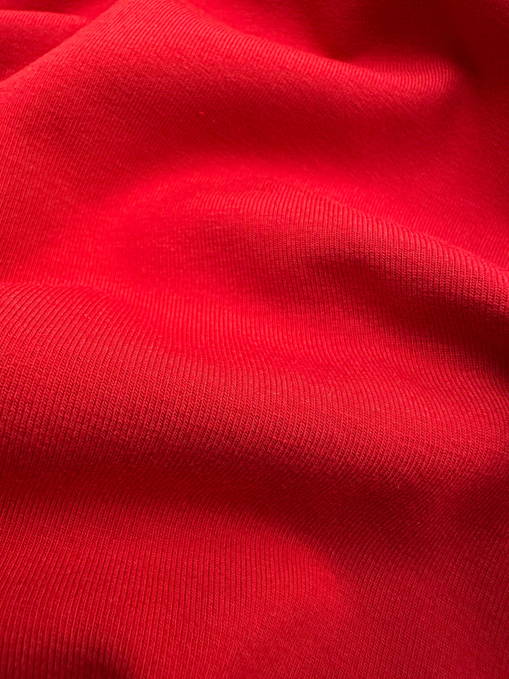 Close-up of vibrant Cotton Lycra in Goji Berry red from Super Cheap Fabrics, featuring a smooth, ribbed texture. The gentle folds highlight the supple nature of this medium-weight fabric, perfect for crafting stylish bodycon dresses. Width: 170cm.