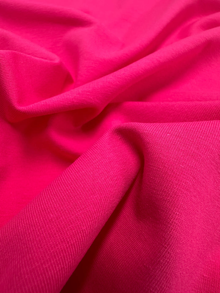 Close-up of Super Cheap Fabrics' Cotton Lycra in Fandango Pink, showing its soft, textured surface with gentle folds. The fabric's cotton lycra blend catches light beautifully, enhancing its smooth and supple appearance—ideal for crafting stunning bodycon dresses. Width: 160cm.