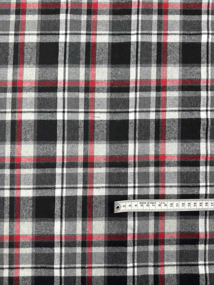 A versatile fabric from Super Cheap Fabrics named "Suiting - Tartanic - 147cm" with a black, white, and red plaid pattern is displayed. A white measuring tape marked with measurements in centimeters from 1 to 15 and printed with the text "MADE IN ITALY" is placed on the fabric.